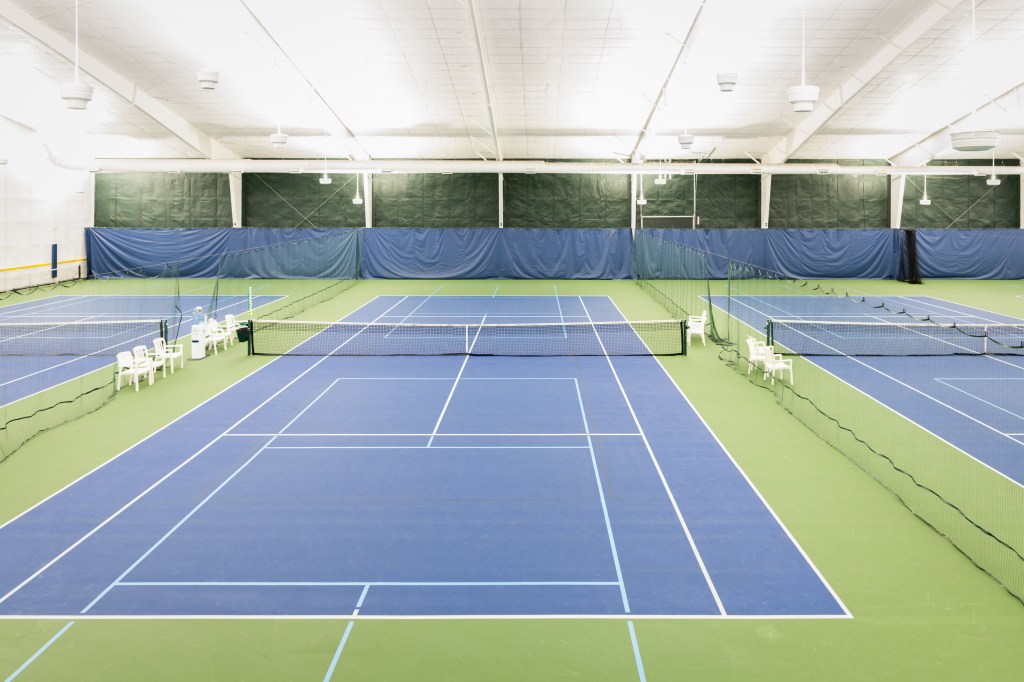Indoor tennis courts with blue playing surface and green surround