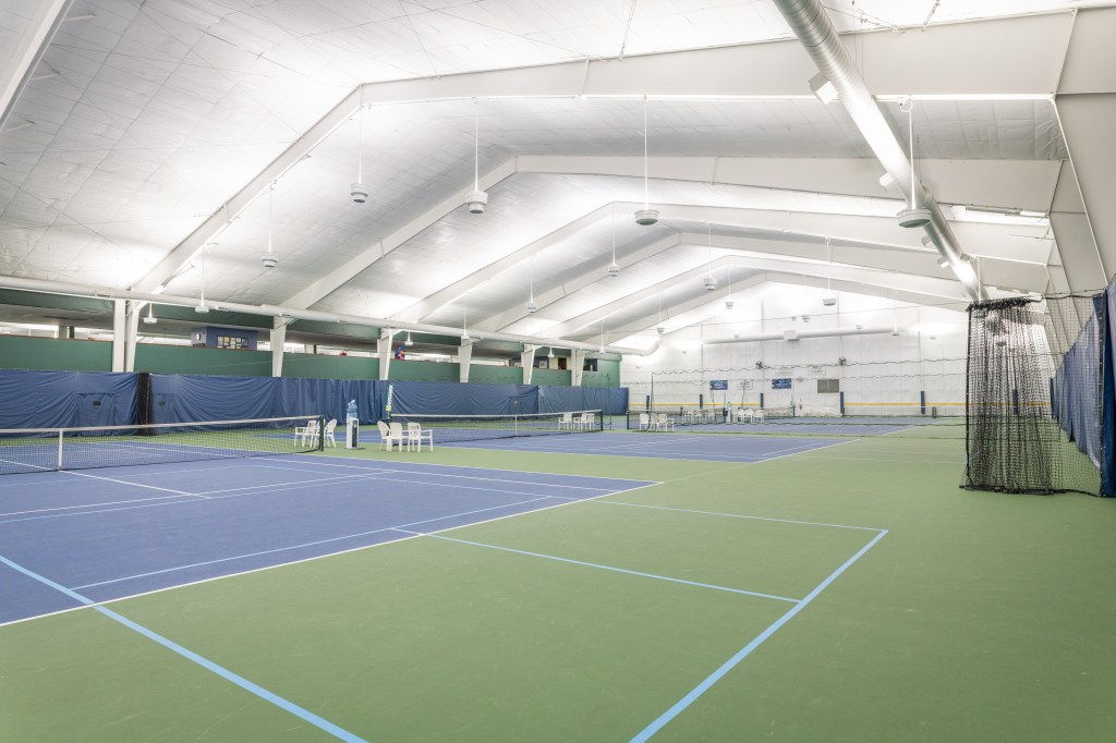 Wide view of the indoor tennis courts under a high, brightly lit ceiling